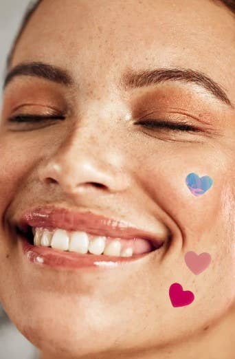 Close-up of a woman's face with closed eyes, smiling, and heart-shaped stickers on her cheek.