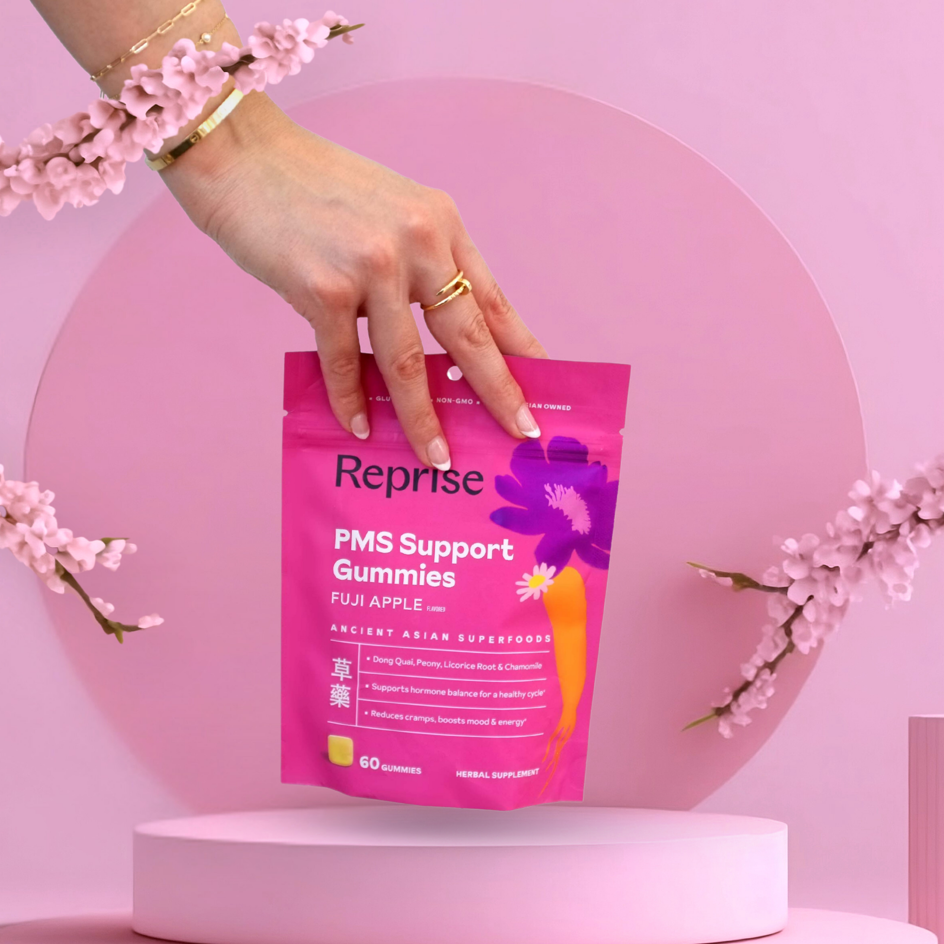 Hand holding a pink 'Reprise' PMS Support Gummies package against a pink background with floral elements.