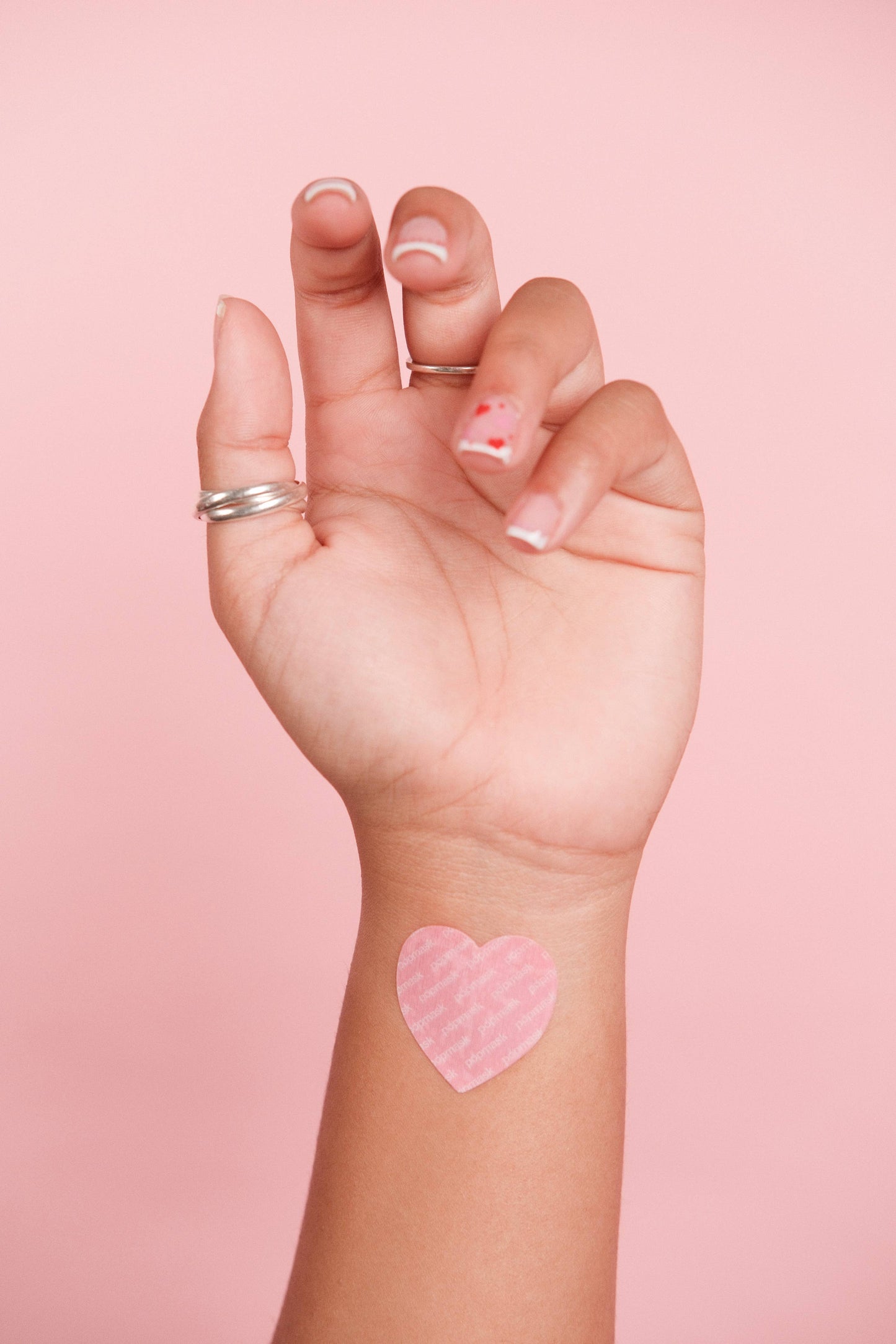 Hand with a pink heart-shaped sticker on a pink background