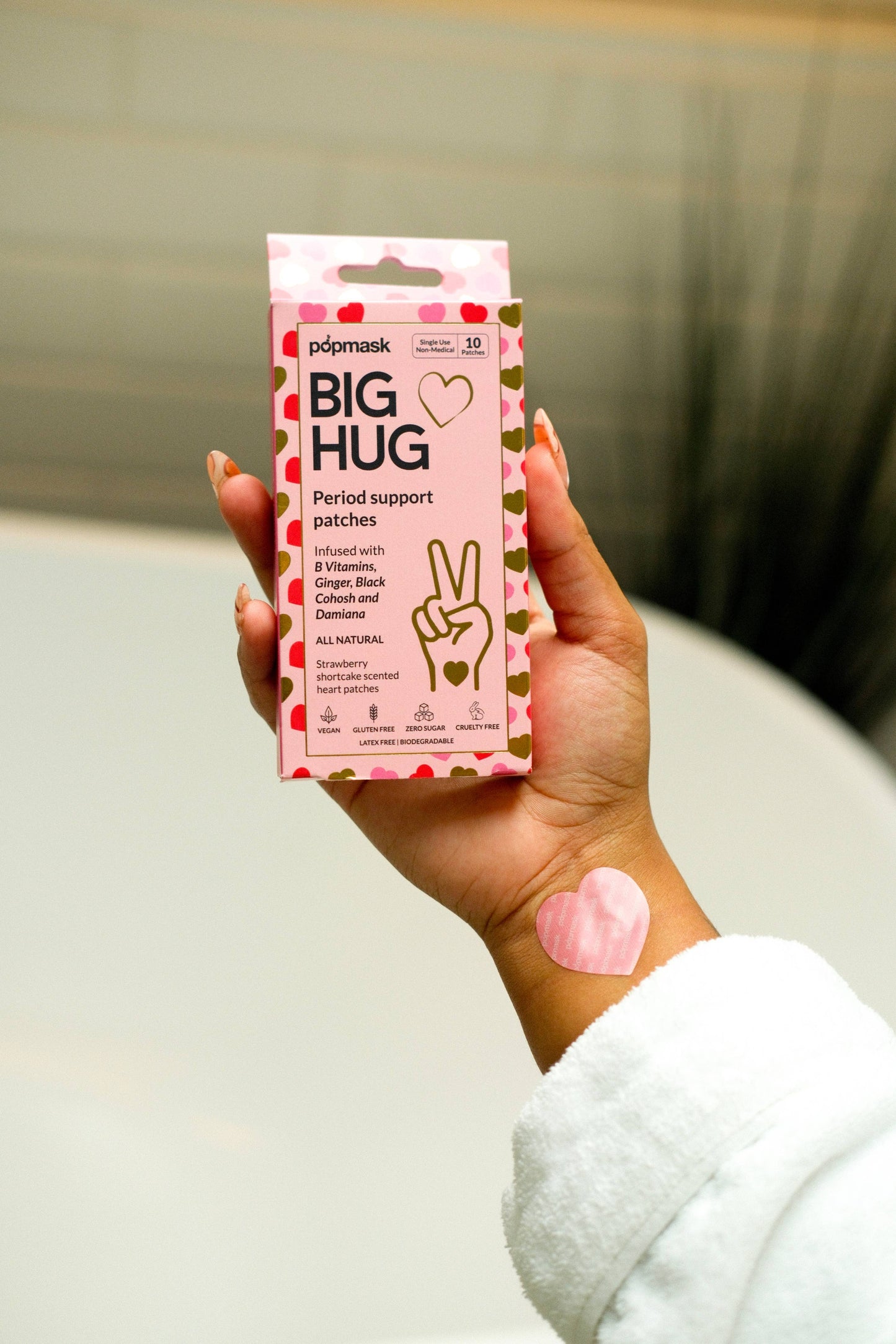 Hand holding a pink box of 'Big Hug' period support patches with a visible patch on the wrist.