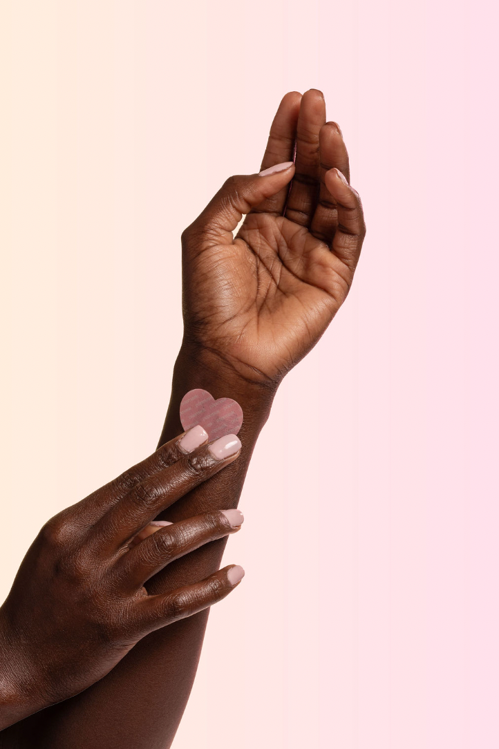Two black hands with heart-shaped vitamin patches on a pink background
