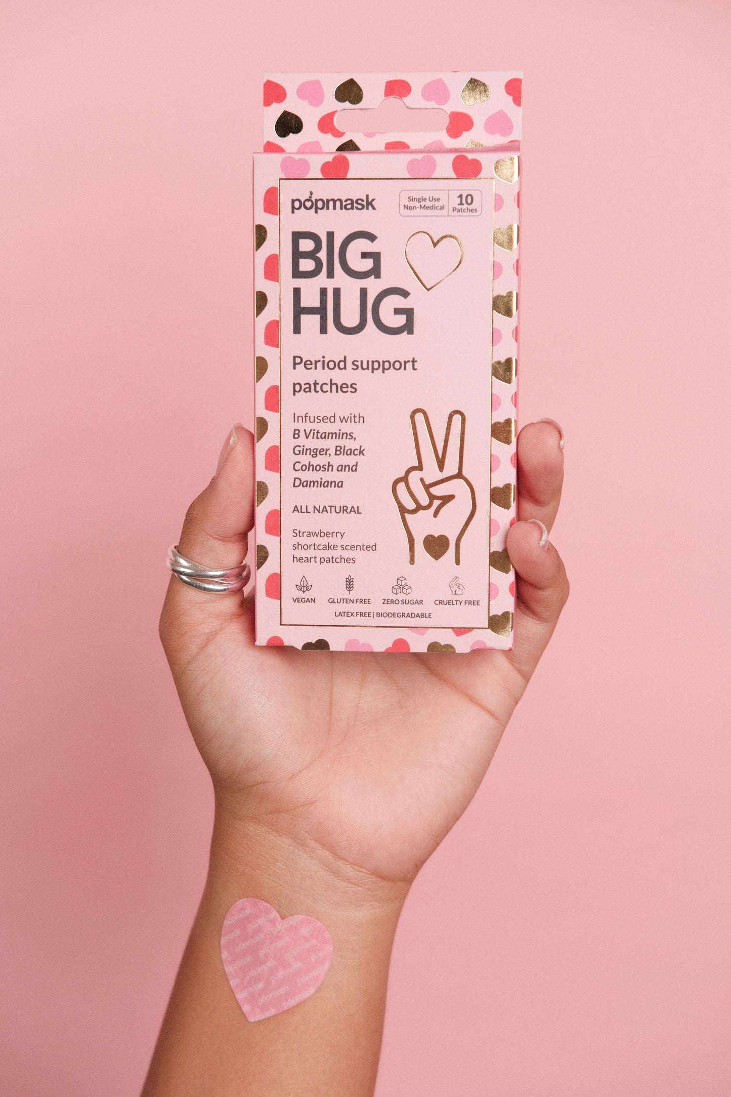 Hand holding a box of popmask BIG HUG period support patches against a pink background
