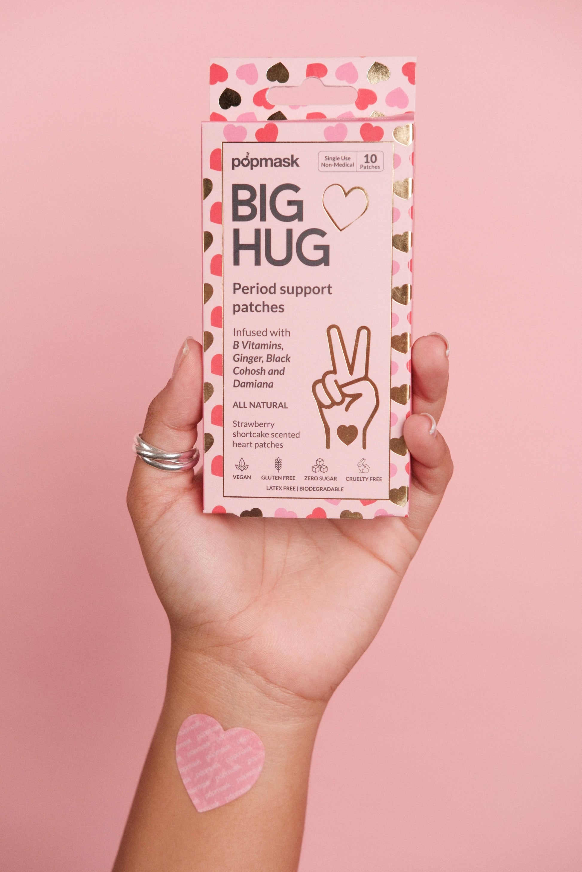 Hand holding a box of popmask BIG HUG period support patches against a pink background
